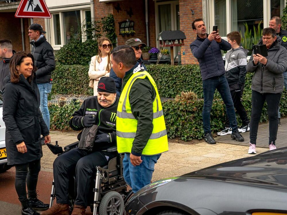 Buurtbewoners kijken toe terwijl een deelnemer naar de auto wordt gebracht