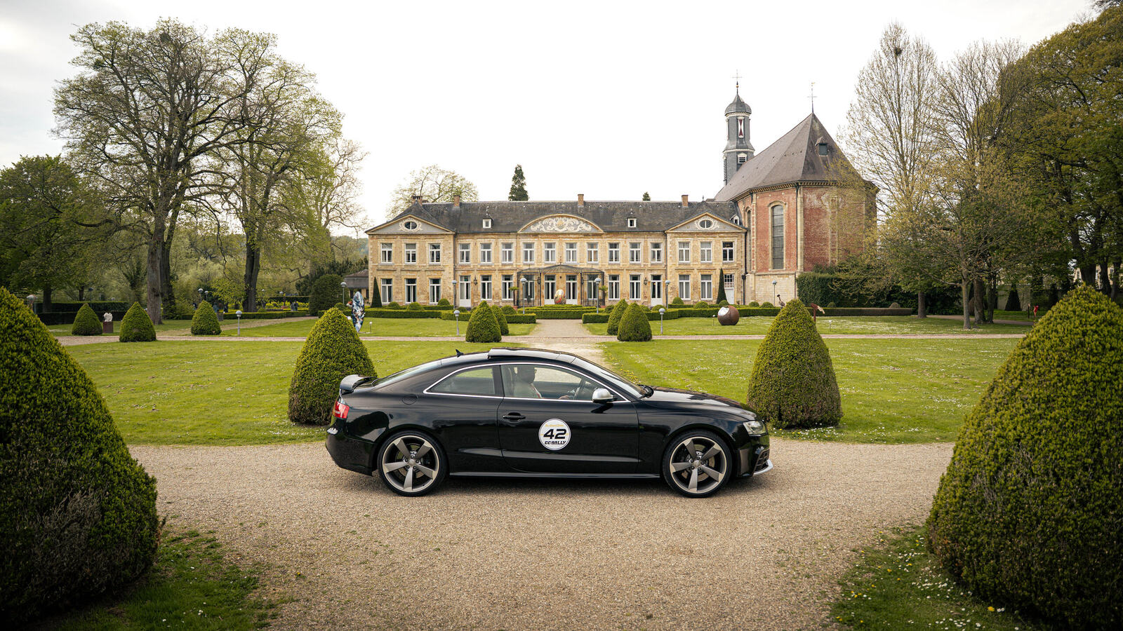 Grey Audi RS6 Avant on the gravel in front of a castle, part of the line-up of a sports car club