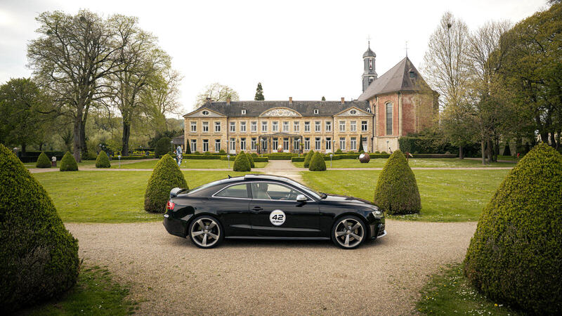 Zwarte Audi met startnummer op het grindpad voor een kasteel, onderweg tijdens een CCRally-rit