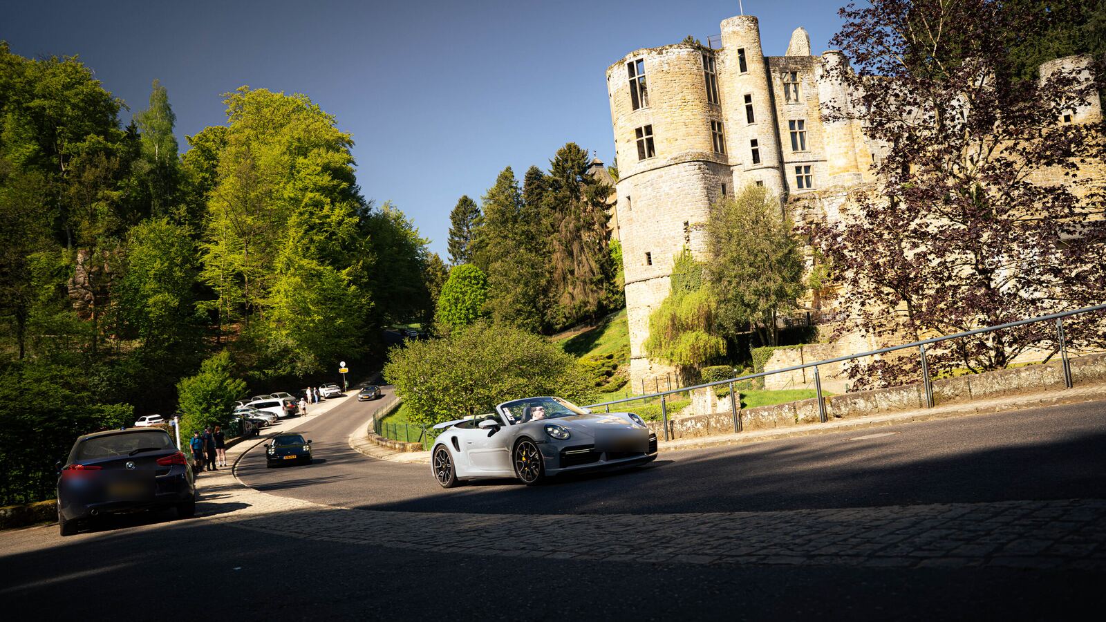 Porsche 911 convertible driving past a castle in Luxembourg during a multi-day supercar tour through Europe